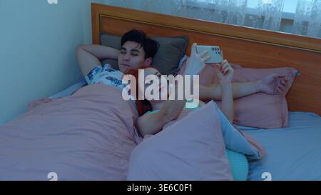Jeune couple utilisant des smartphones ensemble tout en étant allongé dans le lit Banque D'Images