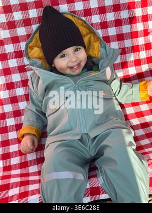 Enfant souriant en combinaison de neige d'hiver sur couverture à carreaux rouge Banque D'Images