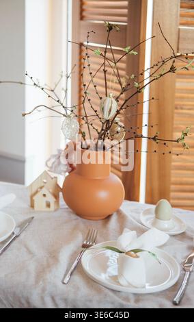 La table met en valeur un vase en terre cuite avec des branches et des ornements, le long d'assiettes et de couverts, avec une petite maison en bois dans un Ar intérieur bien éclairé Banque D'Images
