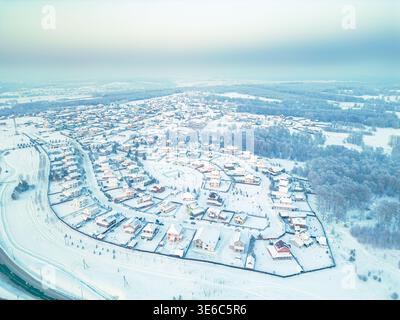 Photographie par drone d'une vaste communauté de chalets avec des rues courbes et des parcelles clôturées près d'une forêt dans un cadre rural enneigé, mise au point sélective Banque D'Images
