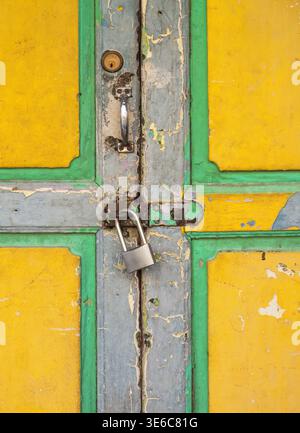 Gros plan de la vieille porte en bois jaune avec peinture pelable, poignée en métal, trou de serrure et cadenas argenté sur garniture vert-bleu Banque D'Images