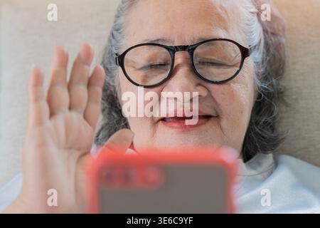 Portrait en gros plan d'une femme asiatique âgée utilisant le téléphone à l'appel vidéo pour saluer sa famille. Concept de style de vie plus ancien. Mise au point sélective. Banque D'Images