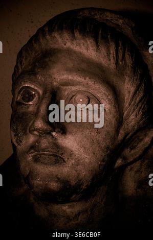 Tarquinia, Latium, Italie : visage sculpté en bronze-rouge avec les yeux fixes d'un jeune citoyen masculin de l'ancienne Tarchuna étrusque ou Tarchna. Une partie de l'effigie couchée sur sarcophage ou couvercle de poitrine de tombeau de nécropole, parmi beaucoup actuellement exposés dans le musée archéologique de Tarquinia. Les vestiges étrusques sont classés au patrimoine mondial de l'UNESCO. Illustration numérique à partir d'une photographie originale. Banque D'Images