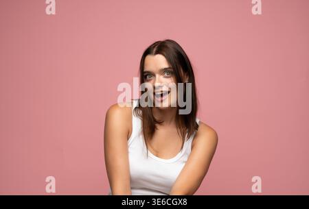 Jeune femme s'amusant, surpris et heureux, exprimant des émotions positives sur un fond rose Banque D'Images