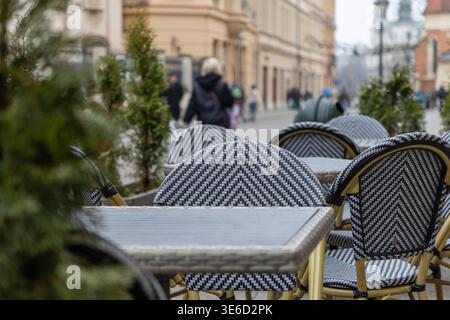 Gros plan de chaises de café vides élégantes à motifs noir et blanc et de tables en osier installées dans une rue européenne, évoquant un dîner urbain serein et attendant g Banque D'Images