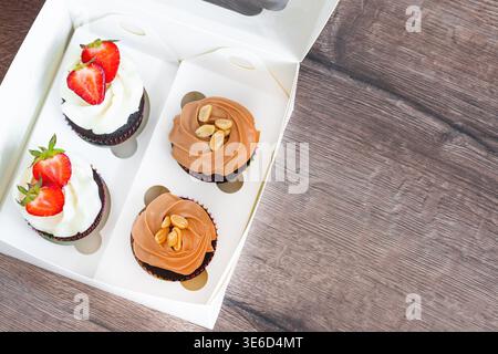 Plan vertical de cupcakes artisanaux au chocolat recouverts de ganache riche et de caramel doré salé. Présenté dans des gobelets en papier marron classiques sur un dos sombre Banque D'Images