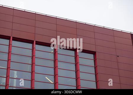Perspective détaillée d'un extérieur de bâtiment moderne avec des panneaux de façade rouge foncé et de grandes fenêtres en verre réfléchissant, idéal pour mettre en valeur l'entreprise Banque D'Images