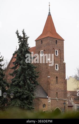 Cracovie, Pologne - 1er décembre 2025 : tour d'église européenne, brique rouge, toit en tuiles, flèche pointue, sapins verts, représentant un archit religieux historique Banque D'Images