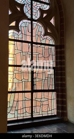 Ancien vitrail avec motif géométrique et arc gothique à l'intérieur du château de Malbork en Pologne. Architecture, histoire et concept patrimonial. Banque D'Images