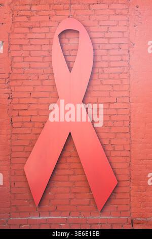Symbole de sensibilisation au VIH et au sida. Ruban rouge sur un fond de briques peintes rouges. Grand ruban rouge sur un mur de briques. Concept de la Journée mondiale de lutte contre le sida Banque D'Images