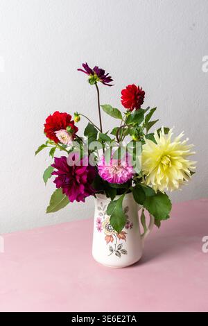 Un vase contient une variété de fleurs fraîches avec différentes couleurs. Les fleurs sont placées sur une table rose. Derrière le vase se trouve un mur Uni dans un roo lumineux Banque D'Images