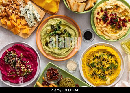 Une planche de charcuterie vibrante présente du brocoli, du curcuma, du houmous classique et de la betterave, associés à des olives, craquelins, et garnitures fraîches, parfait pour Banque D'Images