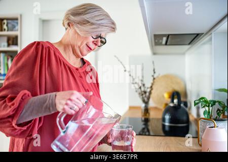 Femme âgée versant de l'eau fraîche dans le verre. Banque D'Images