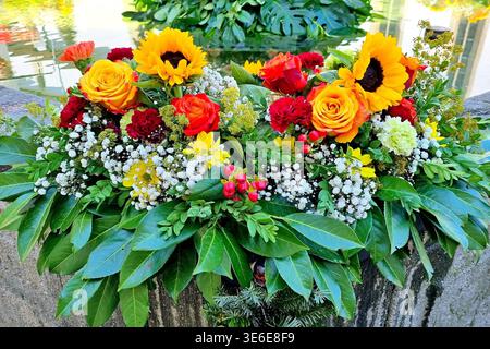 Un arrangement floral vibrant décore la bordure en pierre d'une fontaine. Banque D'Images