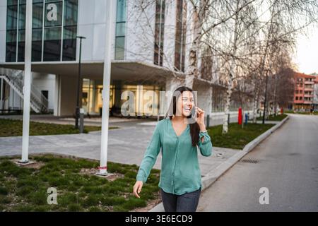 Jeune femme marchant dans la rue et parlant sur un smartphone Banque D'Images