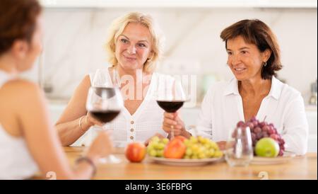 Amis féminins adultes détendus s'amusant à la fête de la maison, partageant des histoires et riant réunis autour de la table avec du vin et des hors-d'œuvre dans la cuisine Banque D'Images