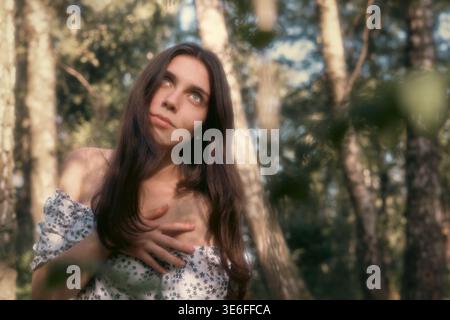 Portrait naturel d'une jeune femme brune dans la lumière chaude des bois avec un avant-plan flou doux. Pose douce, expression calme, beauté et style de vie con Banque D'Images