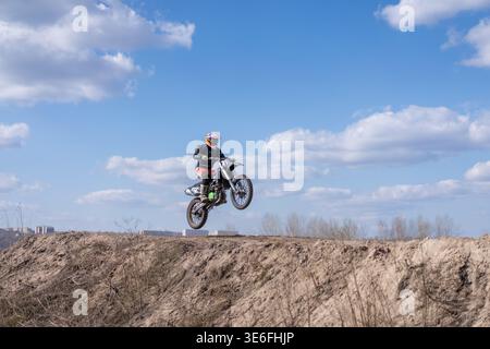 Kharkov Ukraine en mars 2021 pilote effectue un saut sur un vélo enduro sur une piste hors route le ciel a des nuages, et l'arrière-plan montre un paysage urbain. Banque D'Images