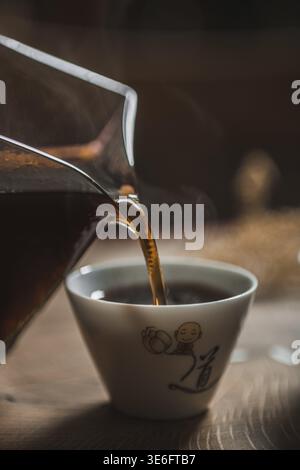 Voici une image rapprochée d'un café riche versé d'un pichet élégant dans une tasse chaude à la vapeur Banque D'Images