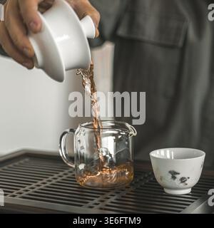 Il s'agit d'un gros plan détaillé de thé étant élégamment versé d'une théière classique dans une cruche en verre et une tasse à thé Banque D'Images
