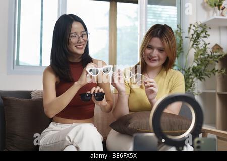 Jeunes femmes s'engageant dans une session de médias sociaux amusante, affichant des lunettes de soleil à la mode tout en profitant de la compagnie de l'autre Banque D'Images