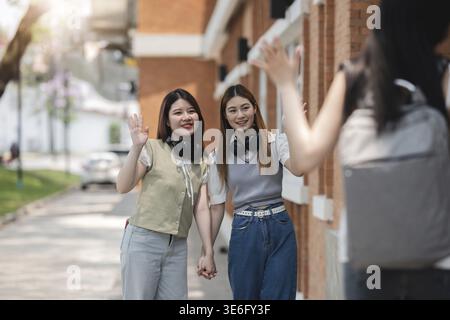 Groupe d'étudiants asiatiques et heureux faisant signe à ses amies saluant ses amies tout en marchant dans le parc Banque D'Images