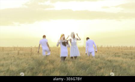 Groupe de jeunes heureux profitant d'une bonne journée sur l'herbe verte au coucher du soleil. Courir groupe d'amis courir sur la prairie, coucher de soleil, silhouette Banque D'Images