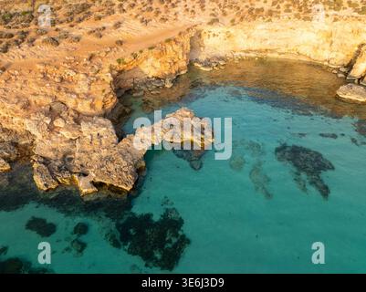 Vue aérienne des eaux turquoises cristallines rencontre des falaises accidentées et ensoleillées dans une étreinte côtière sereine, Blue Lagoon, Comino, Malte. Banque D'Images