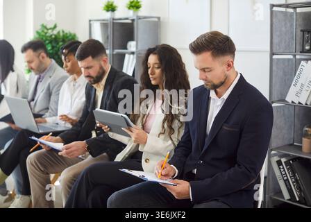 Employés travaillant sur des appareils, prenant des notes assis dans la rangée dans le bureau Banque D'Images