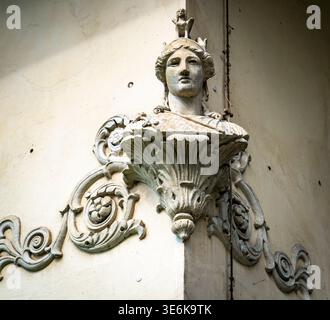 Sculpture en coin de pierre ornée d'une tête féminine avec couronne et parchemins floraux sur la façade du bâtiment historique, vue d'en bas dans la lumière du jour douce. Banque D'Images