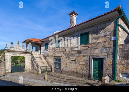 Une maison traditionnelle en pierre de granit avec volets et portes verts dispose d'une passerelle en pierre ornée et d'un escalier extérieur sous un ciel bleu clair. Banque D'Images