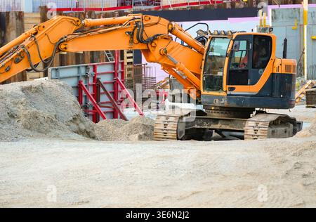 Excavatrice de terrassement travaillant sur le chantier de construction du bâtiment avec pile de terre. Banque D'Images