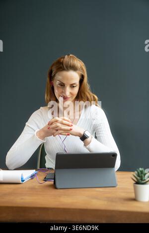 une femme assise à son bureau avec une tablette participant à une réunion en ligne, ou une femme utilisant un module d'apprentissage à distance Banque D'Images