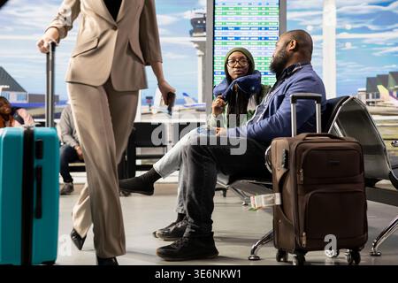 Les voyageurs de couple noir attendant l'embarquement dans le salon de l'aéroport, les gens socialisant excités au sujet des vacances de voyage international pour le départ. Couple avec bagages relaxant sur banc. Banque D'Images