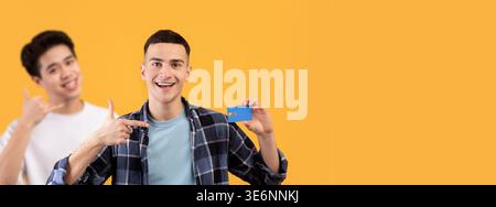 Happy Millennial Guy montre carte de crédit tout en promouvant Contactless Payment dans Studio Banque D'Images