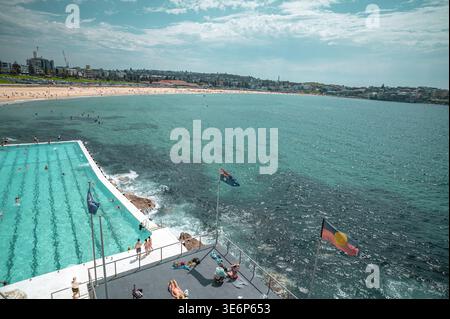 Vue panoramique sur la piscine des icebergs de Bondi et la plage de Bondi avec les drapeaux australien et aborigène flottant au premier plan. Banque D'Images