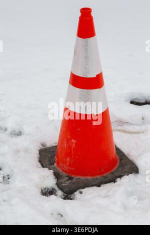 Gros plan d'orange fluorescent avec bandes réfléchissantes blanches circulation en caoutchouc et cône de sécurité de construction en hiver comme la neige au début du printemps, Québec, CA Banque D'Images