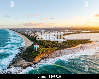 Une perspective aérienne capture le promontoire de point Cartwright, l'entrée de la rivière Mooloolah et une ville côtière tentaculaire pendant un lever de soleil doré vibrant. Banque D'Images