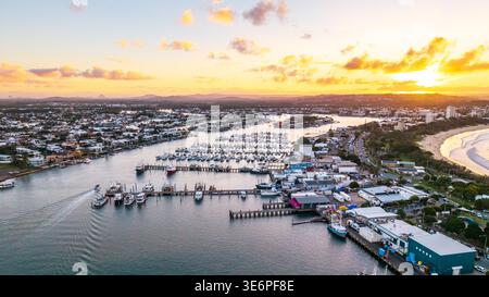 Une vue aérienne capture l'heure dorée à point Cartwright, révélant la marina de la rivière Mooloolah, le port animé et une plage ensoleillée. Banque D'Images