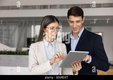 Deux collègues souriants travaillant sur une tâche avec une tablette Banque D'Images