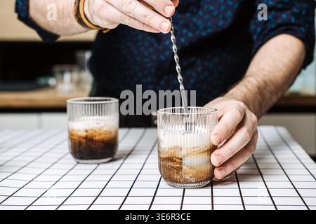 Personne remue le cocktail de café avec la cuillère de bar en métal dans le verre nervuré sur la table de grille. Cocktail de liqueur de café, ingrédients de martini expresso, caféiné Banque D'Images