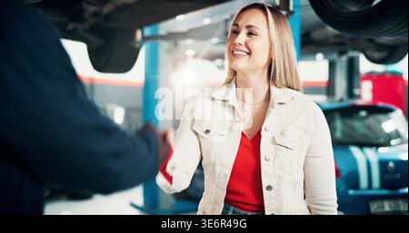 Femme heureuse, client ou poignée de main avec mécanicien pour la réparation, le service automobile ou la réparation dans le garage. Personne féminine, ingénieur ou serrant la main avec le sourire Banque D'Images