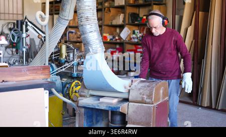 Artisan senior travaillant sur une machine plus épaisse en atelier Banque D'Images