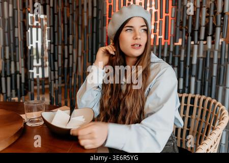 Femme Beret Restaurant jeune dame est assise pensive à une table dans un café élégant profitant du calme seul Banque D'Images