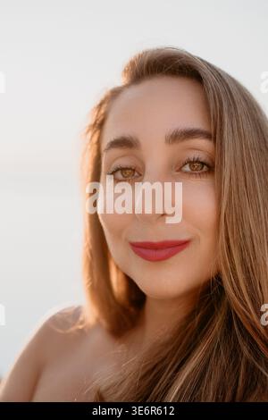 Femme portrait coucher de soleil gros plan d'une jeune femme souriante avec rouge à lèvres rouge profitant de la lueur chaude d'un coucher de soleil en plein air Banque D'Images