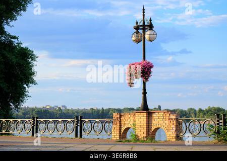 Une scène pittoresque avec un lampadaire noir orné de fleurs roses vibrantes, debout sur une base en brique jaune avec deux arches, entouré d'un Banque D'Images