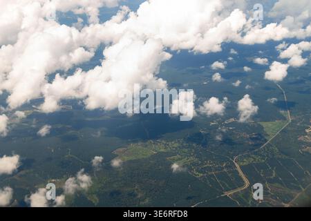 Des nuages blancs et moelleux flottent au-dessus de la forêt verte et du paysage rural avec des routes sinueuses. Vue aérienne depuis la fenêtre de l'avion pendant le vol de jour montrant l'oreille Banque D'Images