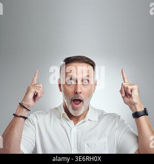 Choqué, mature et portrait avec l'homme pointant en studio pour la publicité sur un fond blanc. Surprise, personne masculine ou modèle avec wow pour Banque D'Images