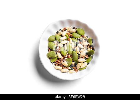 Mélange de graines dans un bol blanc isolé sur fond blanc, vue de dessus, élément de design. Texture des ingrédients alimentaires sains. Graines de citrouille, noir et blanc Banque D'Images