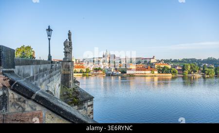 Le pont Charles offre une vue sur le château de Prague. Le soleil brille sur la rivière. Les gens marchent sur le pont, apprécient le paysage et prennent des photos du château et de la ville. Banque D'Images